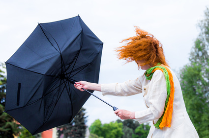 eine Frau mit roten Haaren versucht ihren Regenschirm festzuhalten